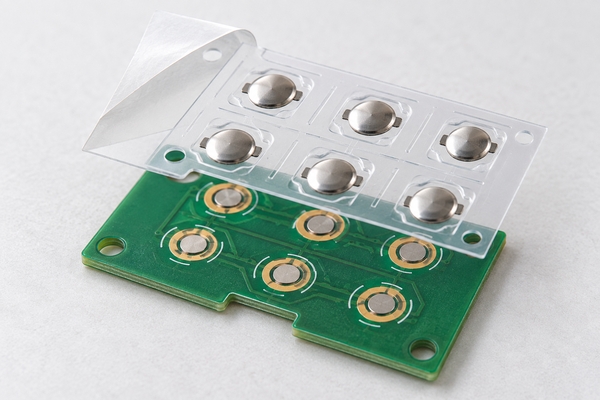 Transparent PET metal dome sheet aligned above matching PCB keypad contacts