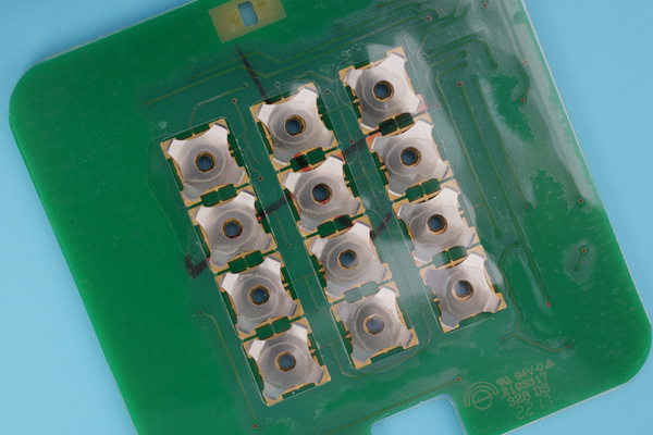 Reference photograph showing four-leg metal domes beneath a clear carrier on a PCB